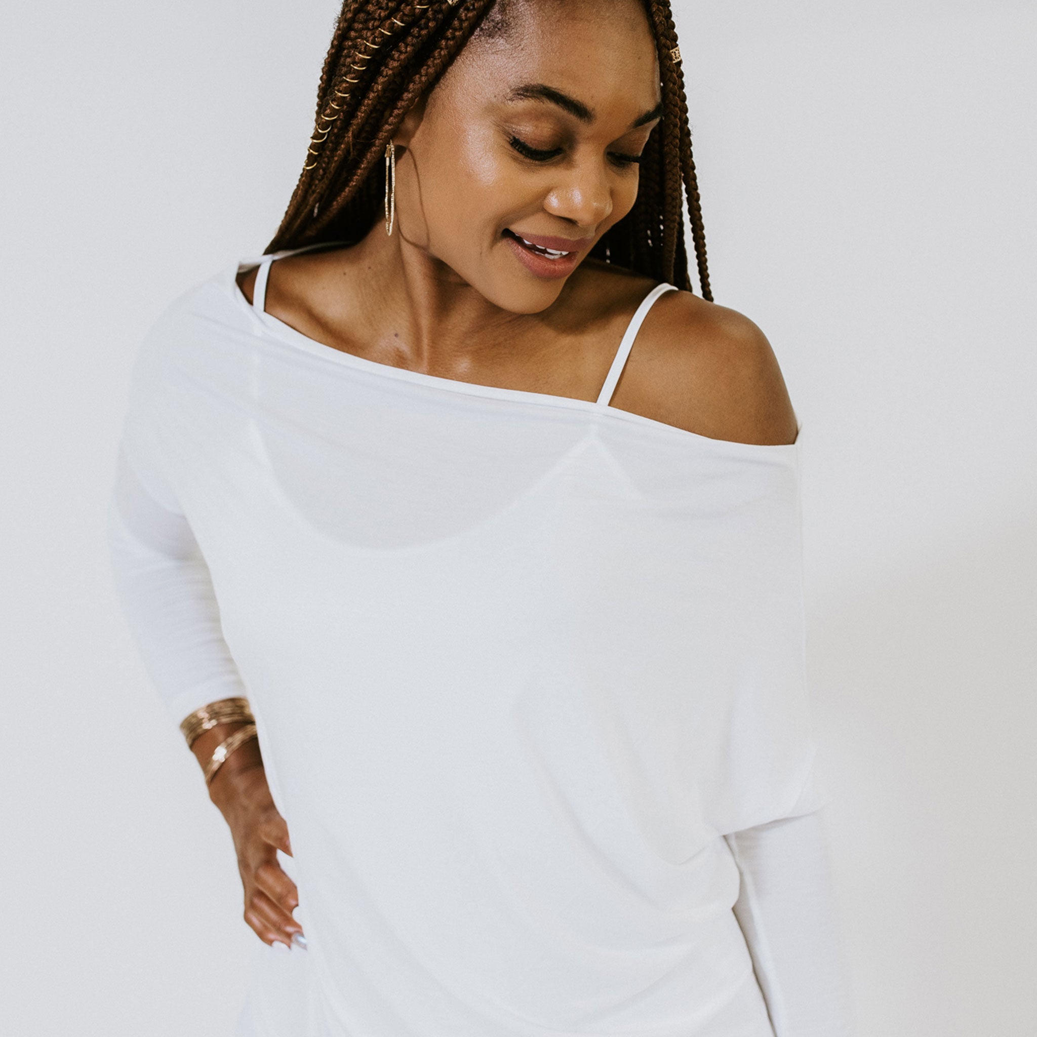 a woman wearing a white long sleeve shirt that drapes off her shoulder, the fabric is shear and you can see her white tank top underneath